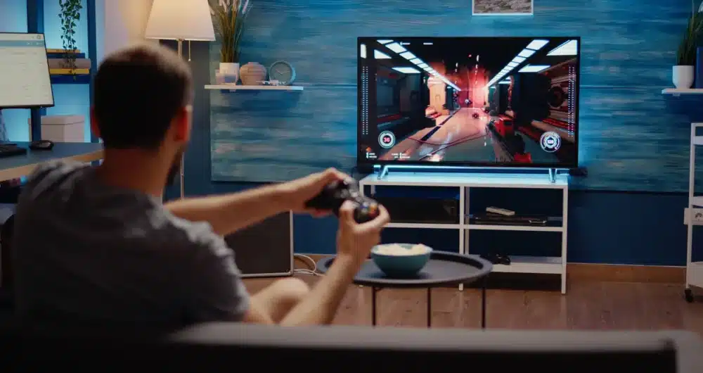 A gamer enjoys an immersive experience on one of the best gaming TVs for PS5 and Xbox, showcasing vibrant graphics and fast response times in a well-lit home setting.