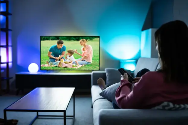 Une femme regardant une Smart TV sur un canapé dans un salon moderne avec un éclairage d'ambiance coloré.